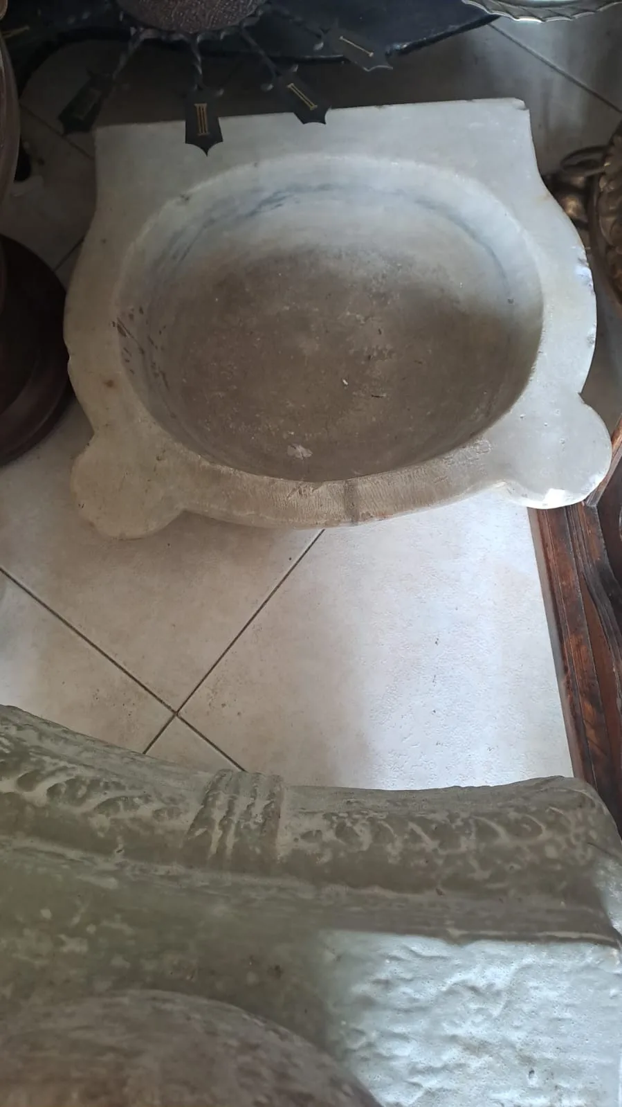 Acquasantiera in marmo bianco con vasca tonda e bordo sagomato, appoggiata a terra in negozio