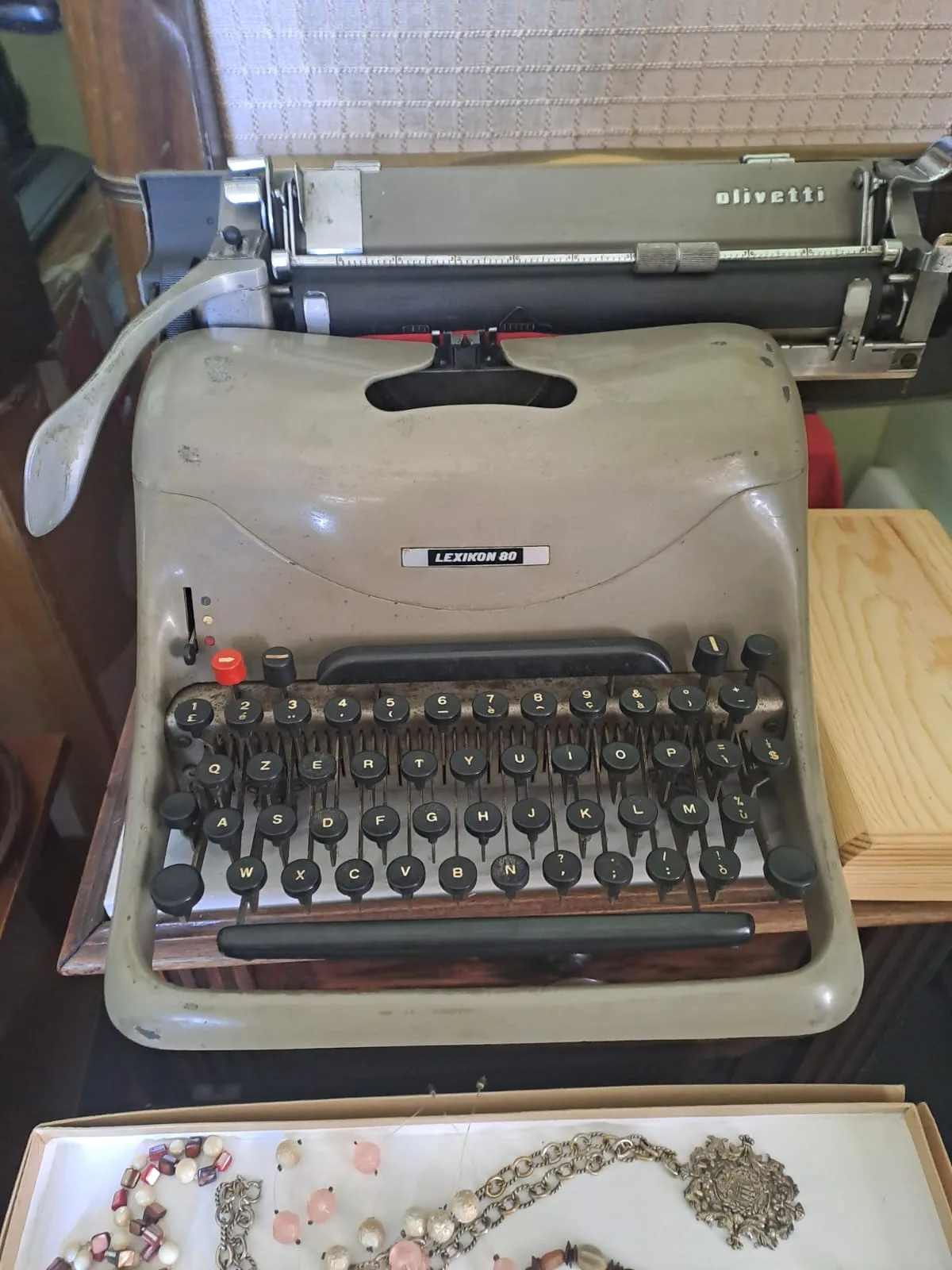 Macchina da scrivere Olivetti Lexikon 80 accanto a un vassoio di collane e spille d'epoca