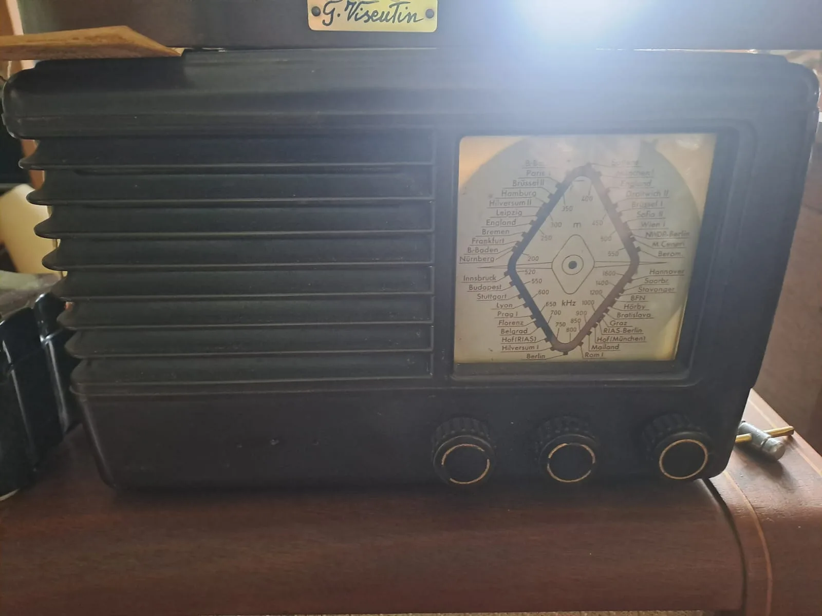 Radio a valvole in bachelite scura con griglia a lamelle e scala parlante illuminata con le stazioni europee